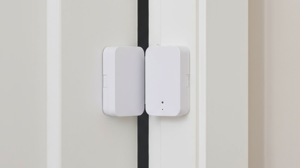 Sensor de contacto para puertas como disparador alternativo Una foto en primer plano de un sensor de contacto magnético de dos partes instalado en una puerta blanca y el marco de la puerta.