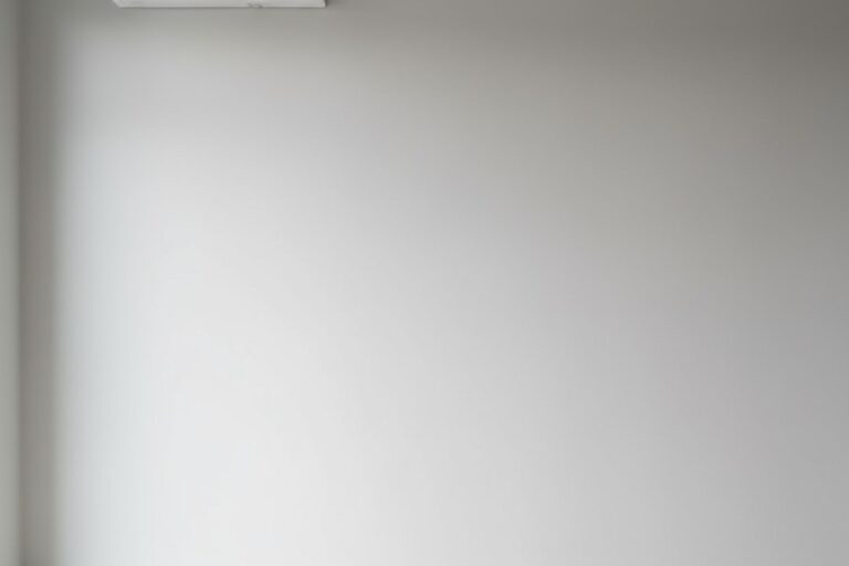 シンプルな白いスプリットエアコンユニットが明るく照明されたモダンな部屋の淡い灰色の壁に高く取り付けられている。