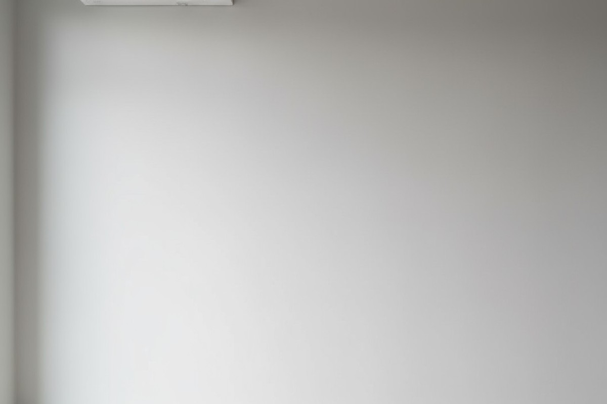 一台極簡的白色分體空調裝置被安裝在明亮的現代房間內淺灰色牆面上的高處。