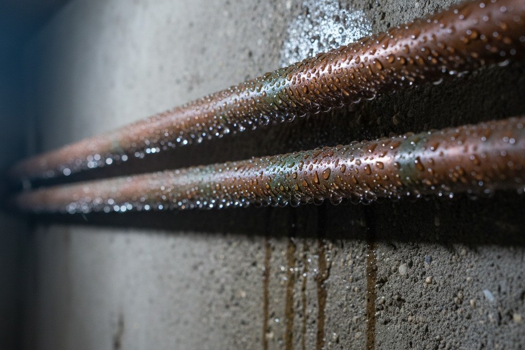 Condensation sur les tuyaux du sous-sol Gros plan sur des tuyaux d'eau en cuivre dans un sous-sol couverts de gouttelettes de condensation importantes contre un mur en béton.