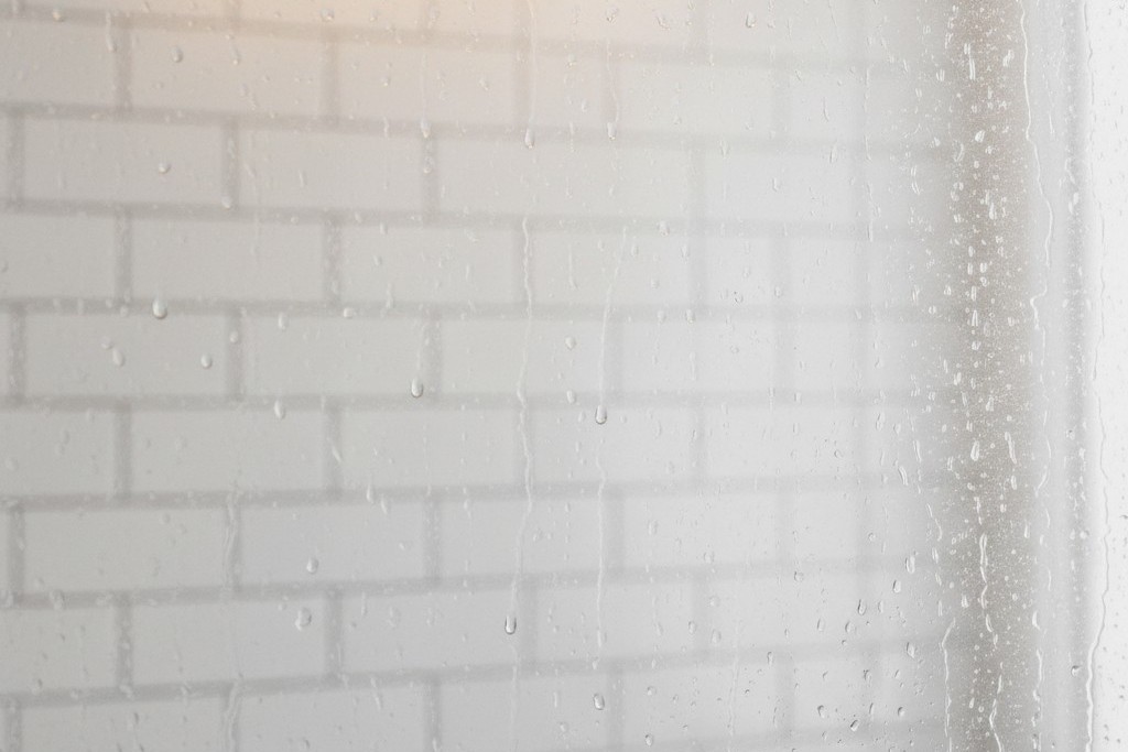 Condensation on bathroom mirror A bathroom mirror heavily fogged with steam, showing water droplets and a blurred reflection of tiled walls.