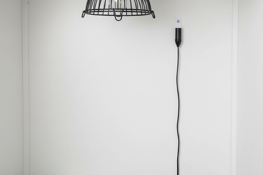 Offset thermostat probe mounting A black thermostat probe secured to the white back wall of a reptile enclosure, positioned several inches to the side of a ceiling-mounted heat lamp cage.